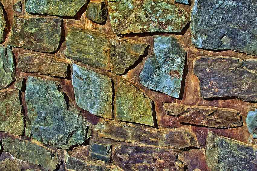 Façade de pierres naturelles irrégulières recouvertes de mousse et patine verte