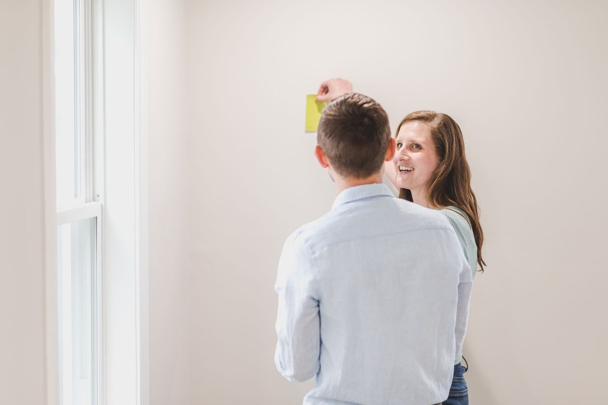 Homme et femme observent un objet jaune contre un mur, près d'une fenêtre lumineuse Homme et femme observent un objet jaune contre un mur, près d'une fenêtre lumineuse
