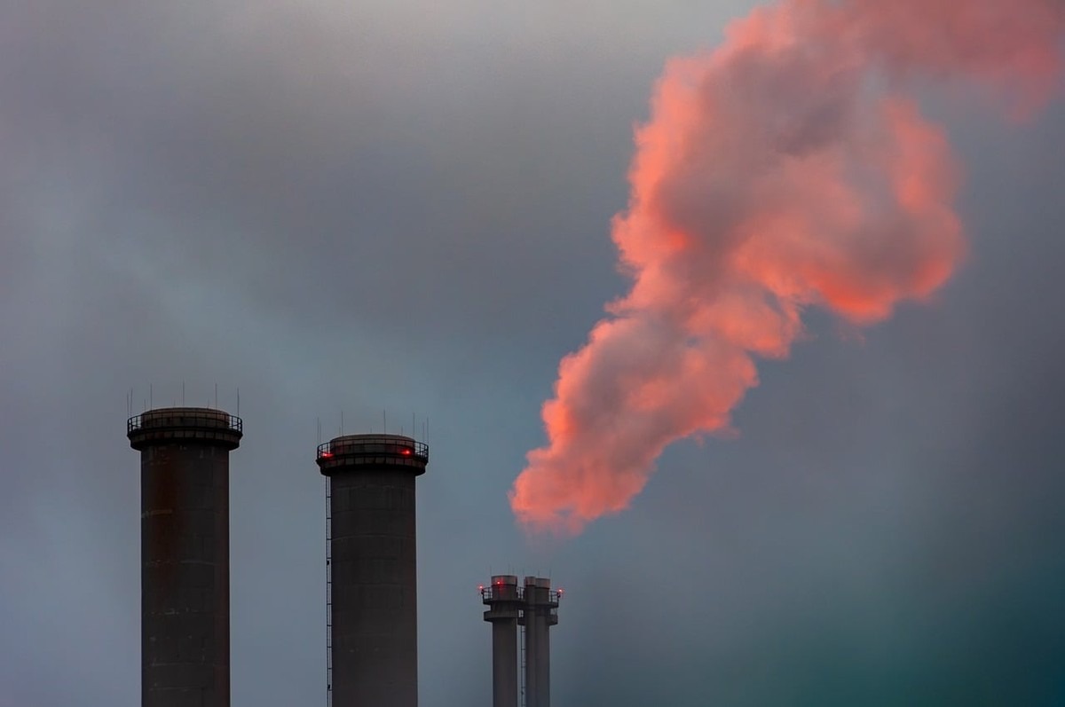 Trois cheminées industrielles émettent une fumée rose pâle dans un ciel gris