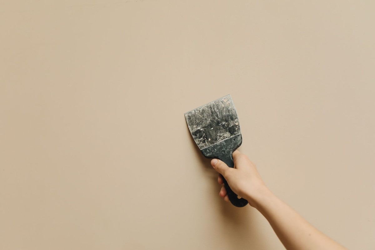 Une main tient un couteau à enduire contre un mur clair Une main tient un couteau à enduire contre un mur clair