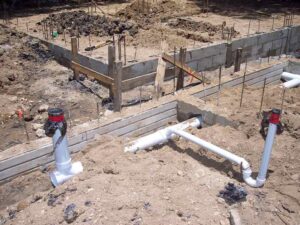 Fondations en béton avec tuyaux PVC et armatures métalliques sur un terrain en terre