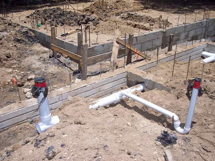 Fondations en béton avec tuyaux PVC et armatures métalliques sur un terrain en terre